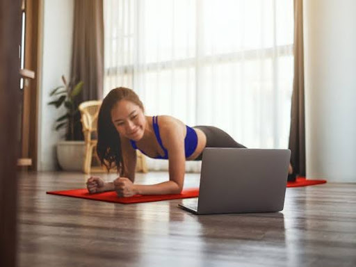 Beautiful asian girl in a plank position while watching workout videos from her laptop.